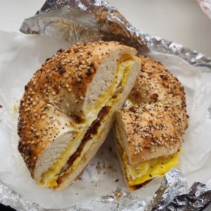 A sliced bagel topped with sesame and poppy seeds, filled with scrambled eggs, sits on tin foil and parchment paper. The vibrant yellow of the eggs is perfectly complemented by the bagel's texture, making it a delightful choice for any catering company Long Island NY can offer.