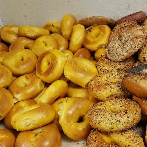 A pile of plain bagels is stacked next to a pile of everything bagels, showcasing their golden-brown allure and speckled charm. Perfect for any occasion, these bagels are a hit with catering services on Long Island, NY.