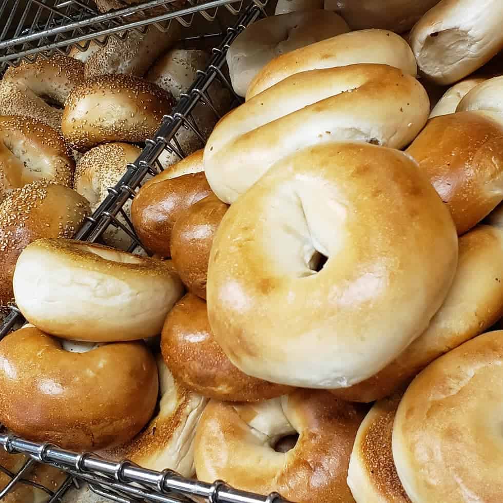 A display of assorted bagels stacked on metal trays by a renowned catering company Long Island NY. The bagels vary in types, with plain and seeded varieties visible, showcasing their golden-brown crusts.