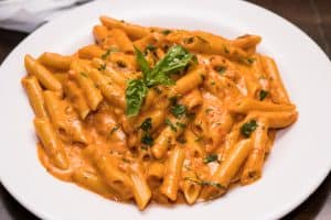 Tabletop shot of a beautifully prepared bowl of penne pasta, garnished with fresh herbs and rich sauce, served at Brendel’s Bagels in Long Island, NY.