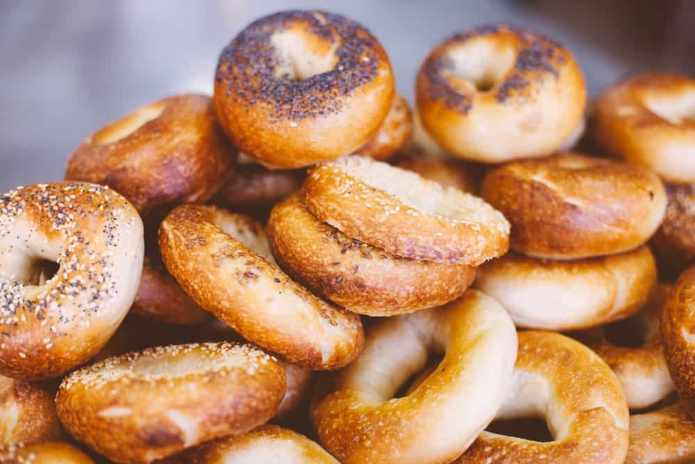 A pile of fresh bagels, some topped with poppy seeds and others with sesame seeds, showcasing a golden-brown crust—a delicious offering from a premier catering company on Long Island, NY.